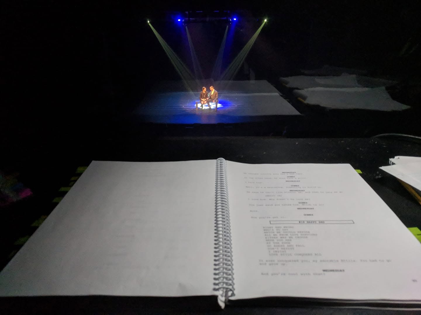 Director's view from the tech table: script in hand, actors lit on stage